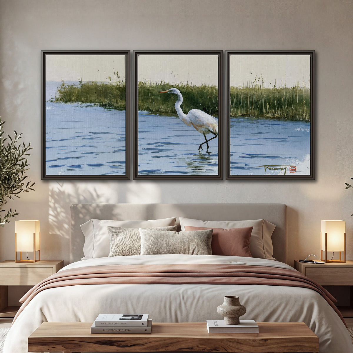 A white heron wading through bright blue water beside green reeds 3 piece framed canvas wall art displayed in a bedroom
