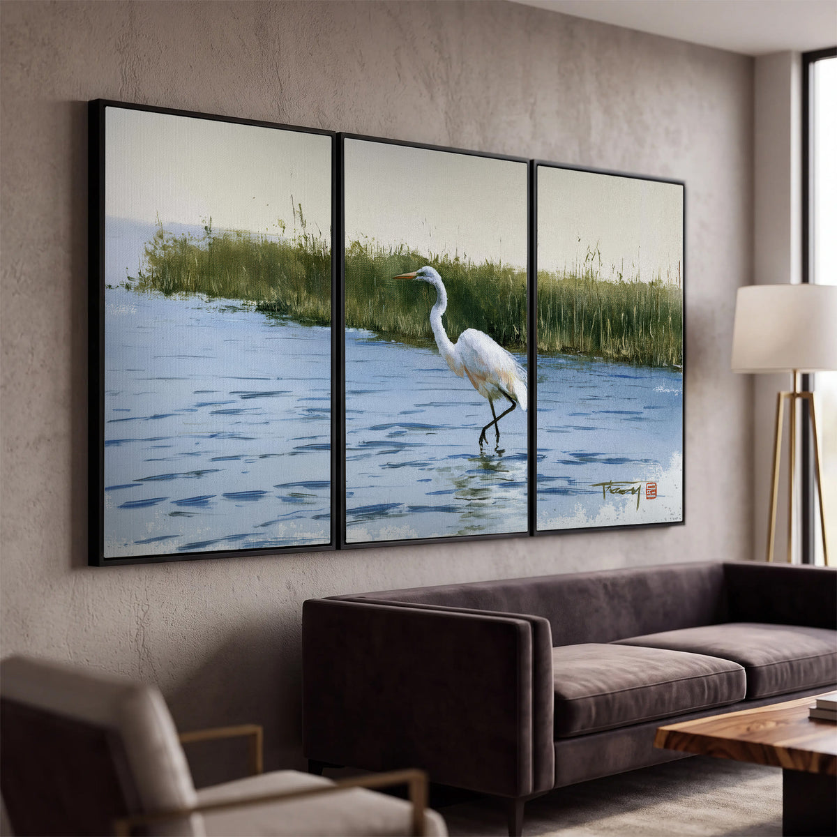 A white heron wading through bright blue water beside green reeds 3 piece framed canvas wall art displayed in a modern living room