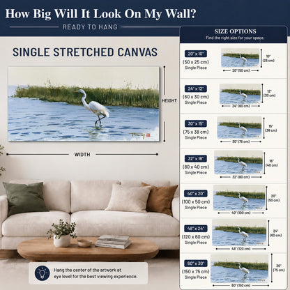 A white heron wading through bright blue water beside green reeds single canvas wall art size guide above a sofa; room view is illustrative