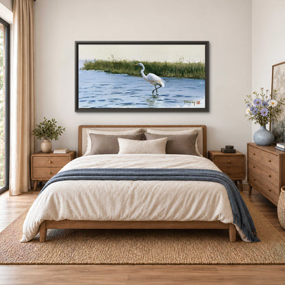 A white heron wading through bright blue water beside green reeds single framed canvas wall art styled in an interior