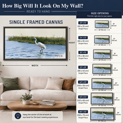 A white heron wading through bright blue water beside green reeds single framed canvas wall art size guide above a sofa; room view is illustrative