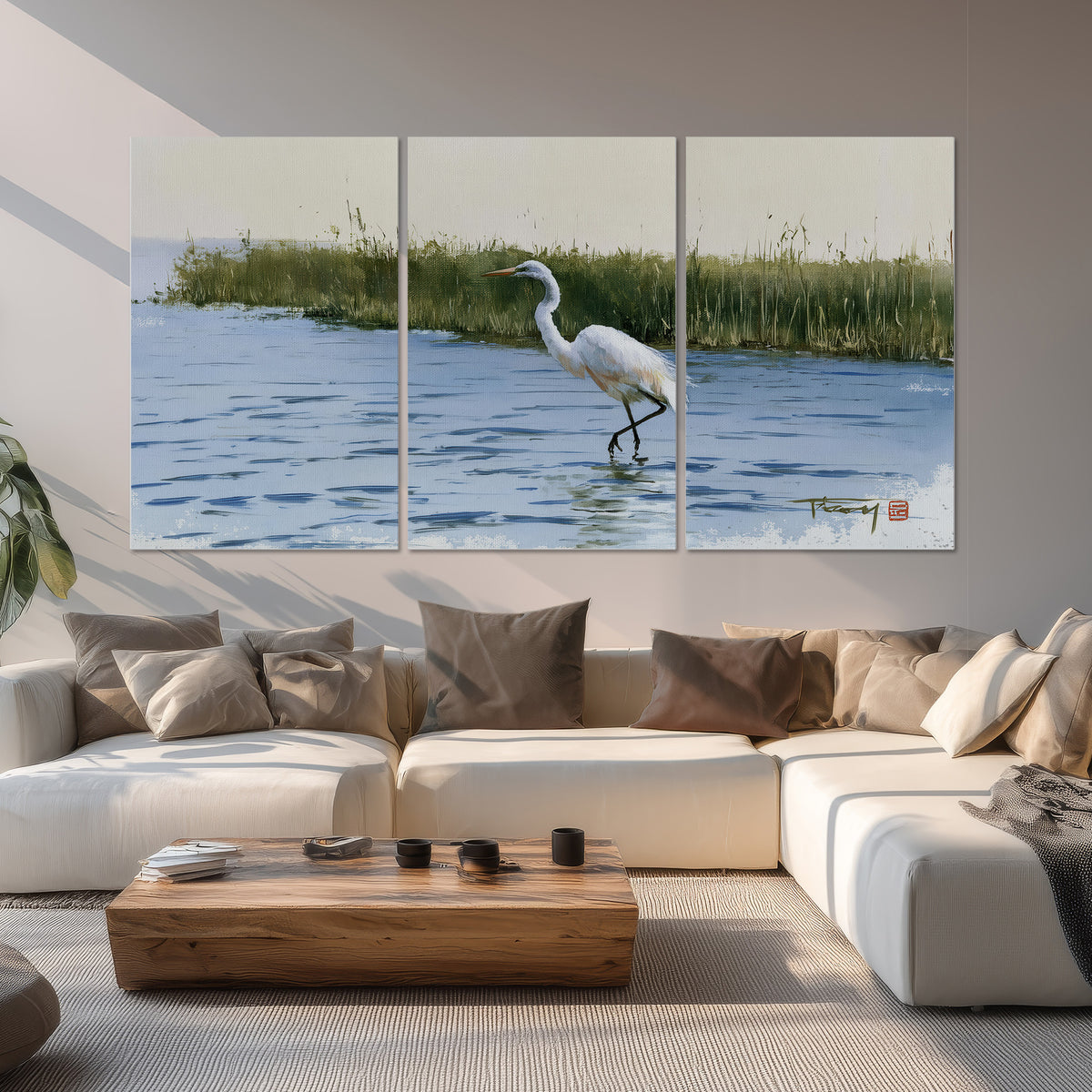 A white heron wading through bright blue water beside green reeds set of 3 poster prints displayed in a living room
