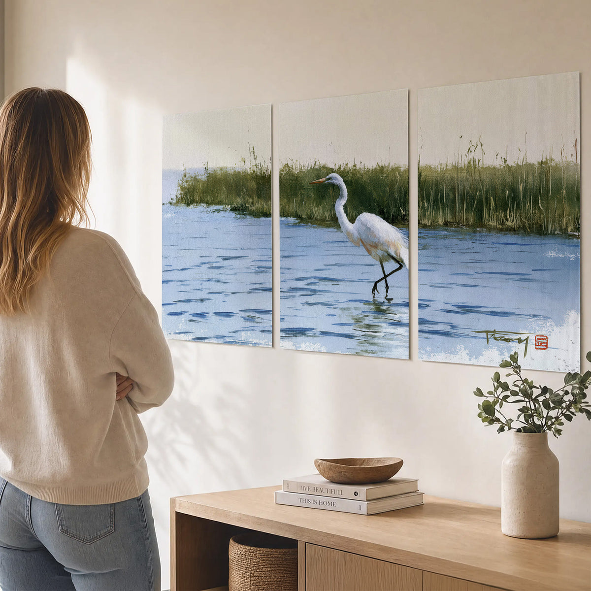 A white heron wading through bright blue water beside green reeds set of 3 poster prints three panel arrangement on a wall