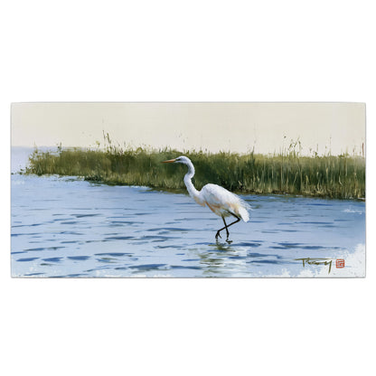A white heron wading through bright blue water beside green reeds single canvas wall art viewed straight on