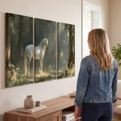 A white unicorn standing beneath arching trees in a softly lit woodland 3 piece canvas wall art three panel arrangement on a wall
