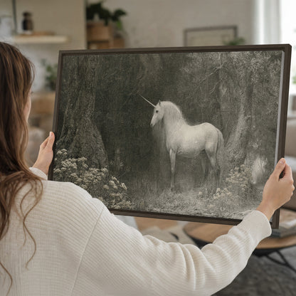 A pale unicorn surrounded by fine gray woodland branches and soft mist single framed canvas wall art held in hands