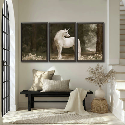 A white unicorn standing in a shadowed forest clearing among dark tree trunks 3 piece framed canvas wall art displayed in a entryway