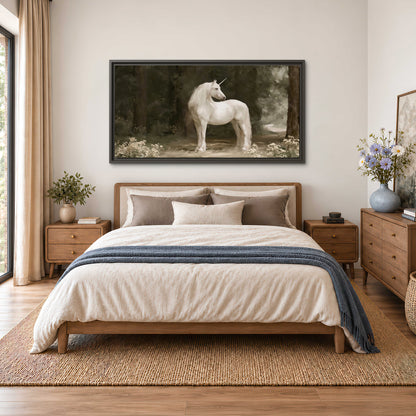 A white unicorn standing in a shadowed forest clearing among dark tree trunks single framed canvas wall art styled in an interior