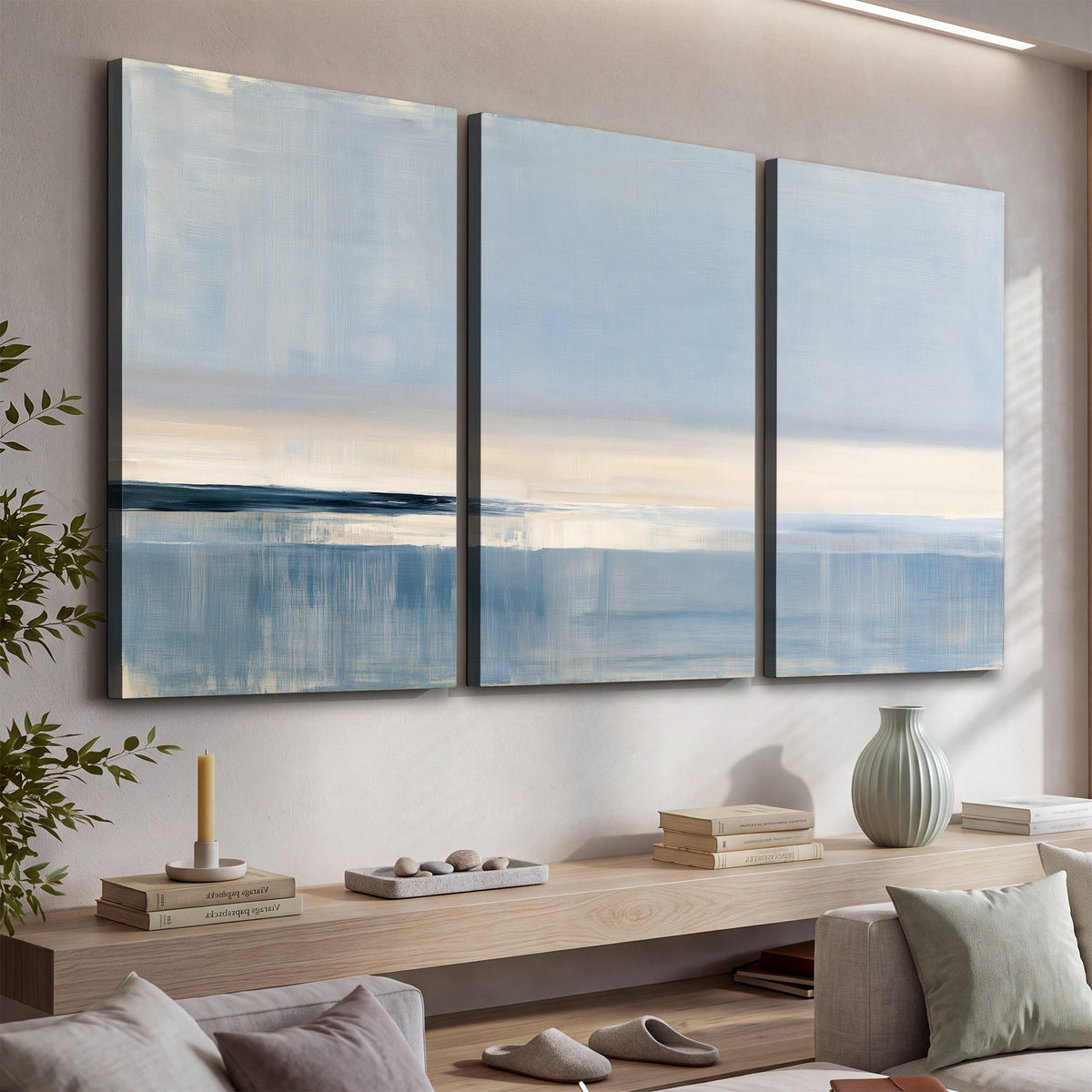 A minimal blue seascape with a pale horizon and soft vertical reflections 3 piece canvas wall art displayed in a console
