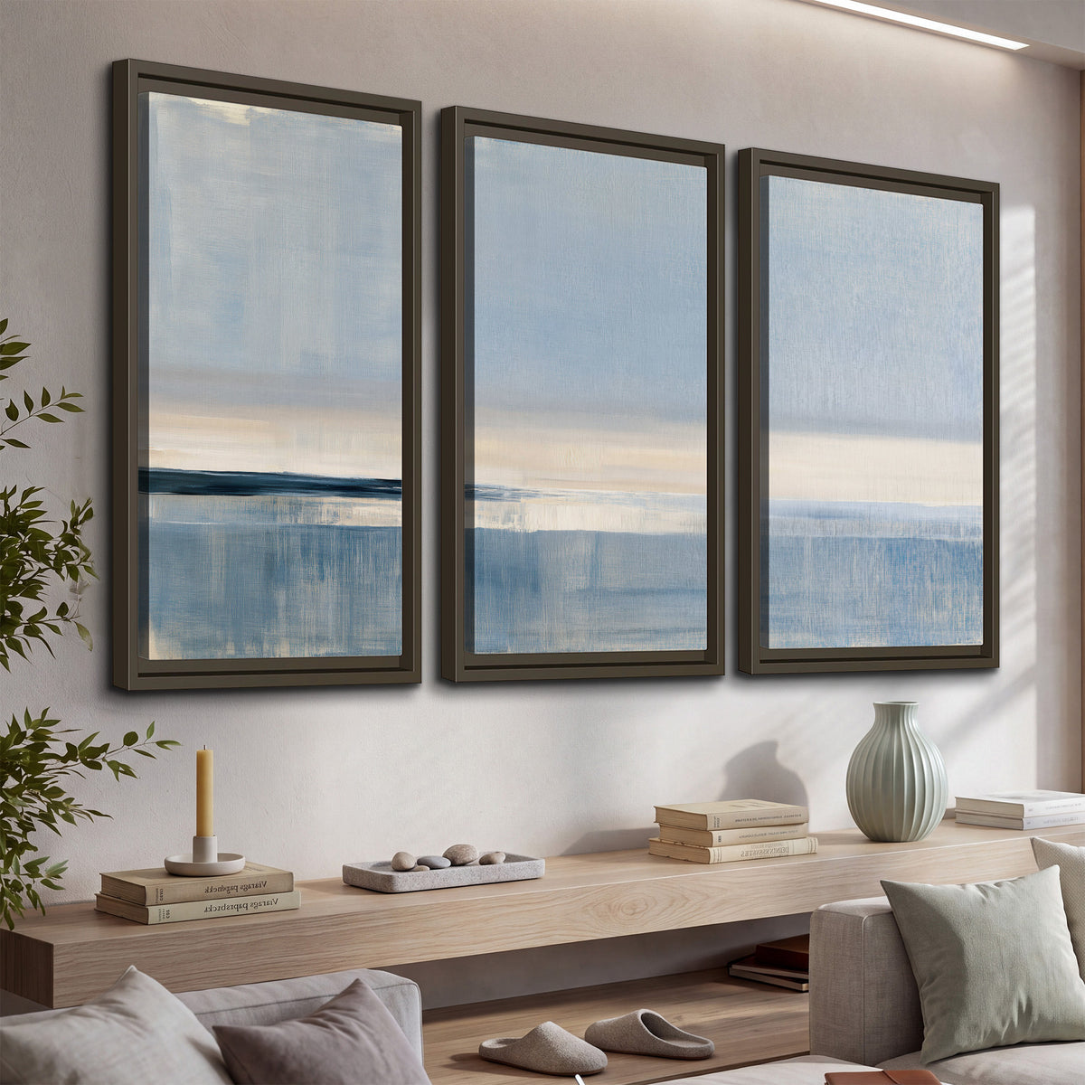 A minimal blue seascape with a pale horizon and soft vertical reflections 3 piece framed canvas wall art displayed in a console