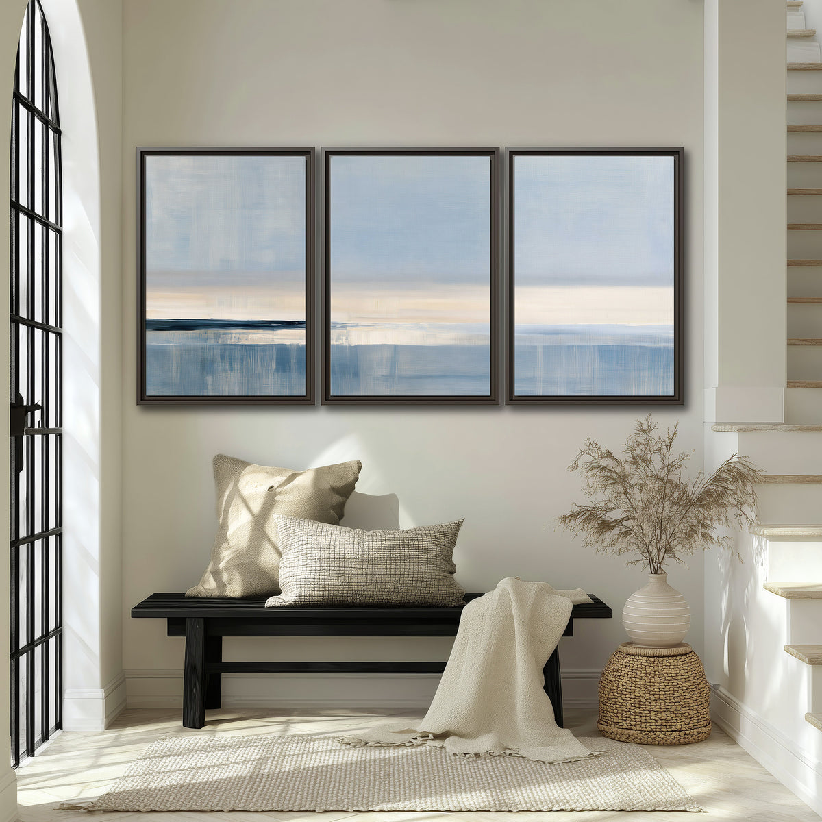 A minimal blue seascape with a pale horizon and soft vertical reflections 3 piece framed canvas wall art displayed in a entryway