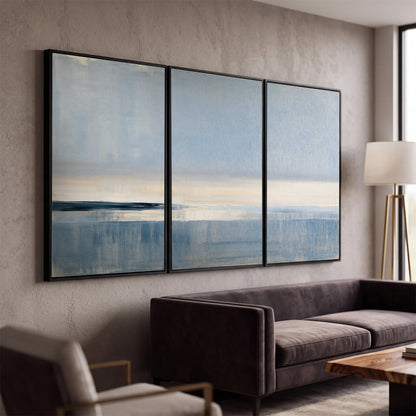 A minimal blue seascape with a pale horizon and soft vertical reflections 3 piece framed canvas wall art displayed in a modern living room