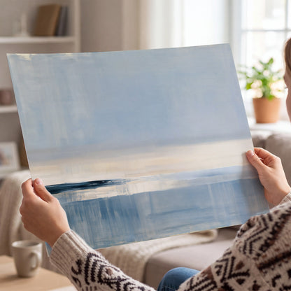 A minimal blue seascape with a pale horizon and soft vertical reflections single poster print held in hands