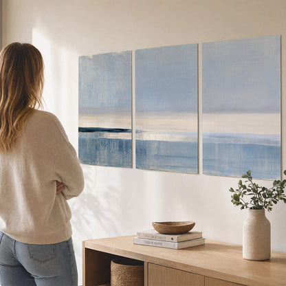 A minimal blue seascape with a pale horizon and soft vertical reflections set of 3 poster prints three panel arrangement on a wall