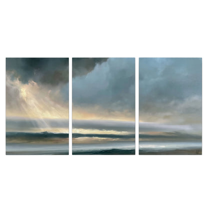 Dramatic blue-gray storm clouds breaking over a pale strip of ocean light 3 piece canvas wall art viewed straight on