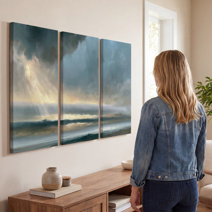 Dramatic blue-gray storm clouds breaking over a pale strip of ocean light 3 piece canvas wall art three panel arrangement on a wall