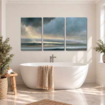 Dramatic blue-gray storm clouds breaking over a pale strip of ocean light 3 piece canvas wall art styled in an interior