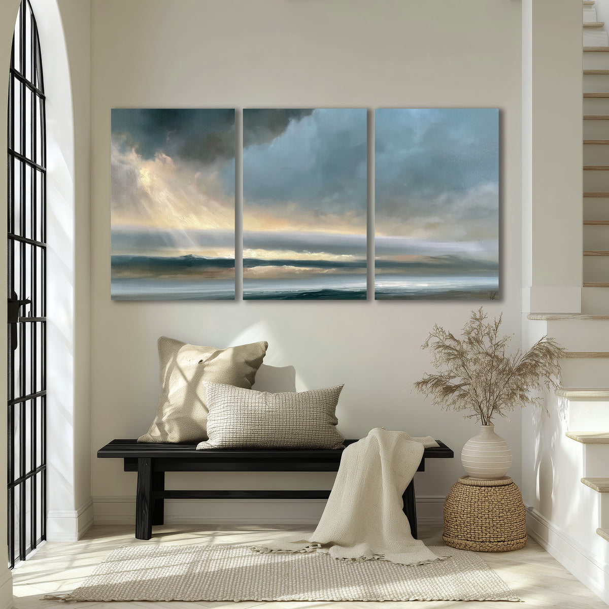 Dramatic blue-gray storm clouds breaking over a pale strip of ocean light 3 piece canvas wall art displayed in a entryway