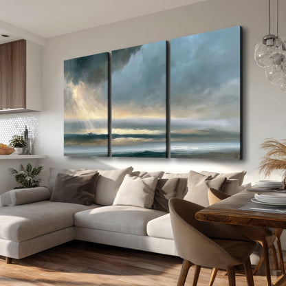 Dramatic blue-gray storm clouds breaking over a pale strip of ocean light 3 piece canvas wall art room and product view