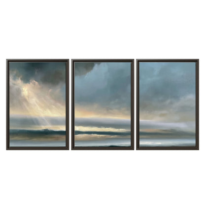 Dramatic blue-gray storm clouds breaking over a pale strip of ocean light 3 piece framed canvas wall art viewed straight on