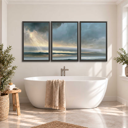 Dramatic blue-gray storm clouds breaking over a pale strip of ocean light 3 piece framed canvas wall art styled in an interior