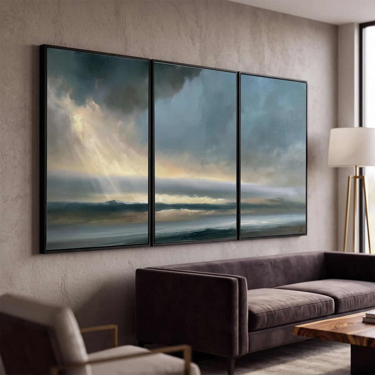 Dramatic blue-gray storm clouds breaking over a pale strip of ocean light 3 piece framed canvas wall art displayed in a modern living room