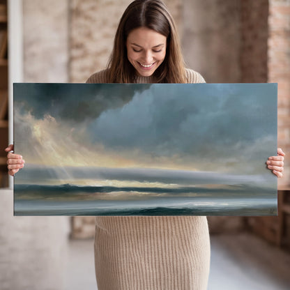 Dramatic blue-gray storm clouds breaking over a pale strip of ocean light single canvas wall art held in hands