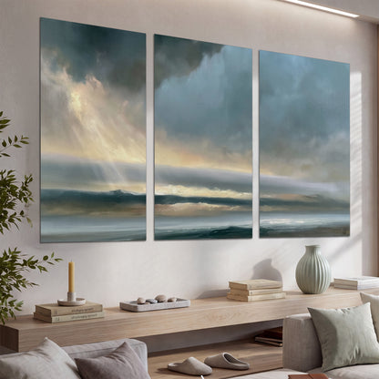 Dramatic blue-gray storm clouds breaking over a pale strip of ocean light set of 3 poster prints displayed in a console