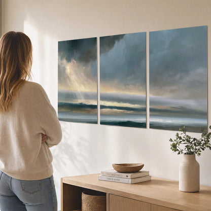 Dramatic blue-gray storm clouds breaking over a pale strip of ocean light set of 3 poster prints three panel arrangement on a wall