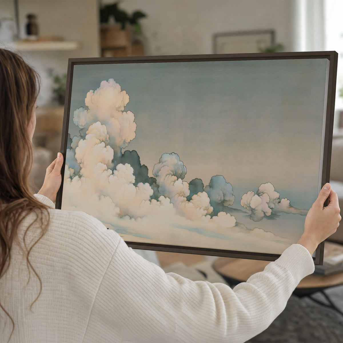 Soft cream clouds gathered low in a muted blue-green sky single framed canvas wall art held in hands