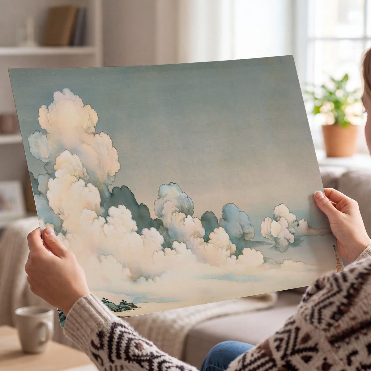 Soft cream clouds gathered low in a muted blue-green sky single poster print held in hands