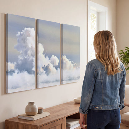 Large white clouds rising through a pale blue sky with gentle warm highlights 3 piece canvas wall art three panel arrangement on a wall