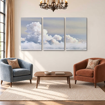 Large white clouds rising through a pale blue sky with gentle warm highlights 3 piece canvas wall art styled in an interior