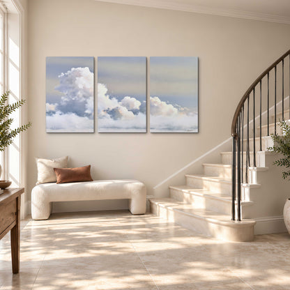 Large white clouds rising through a pale blue sky with gentle warm highlights 3 piece canvas wall art styled in an interior