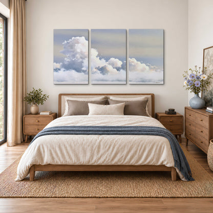 Large white clouds rising through a pale blue sky with gentle warm highlights 3 piece canvas wall art styled in an interior