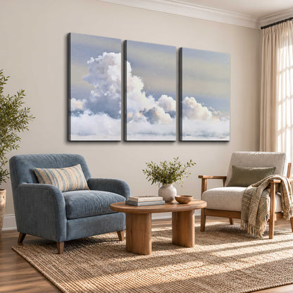 Large white clouds rising through a pale blue sky with gentle warm highlights 3 piece canvas wall art styled in an interior