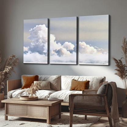 Large white clouds rising through a pale blue sky with gentle warm highlights 3 piece canvas wall art displayed in a rustic living room
