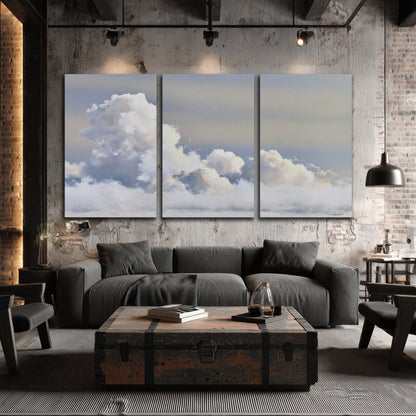 Large white clouds rising through a pale blue sky with gentle warm highlights 3 piece canvas wall art displayed in a industrial room