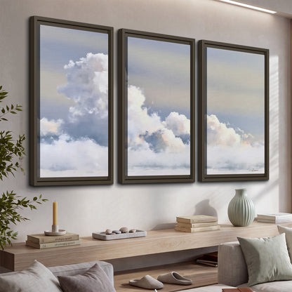 Large white clouds rising through a pale blue sky with gentle warm highlights 3 piece framed canvas wall art displayed in a console