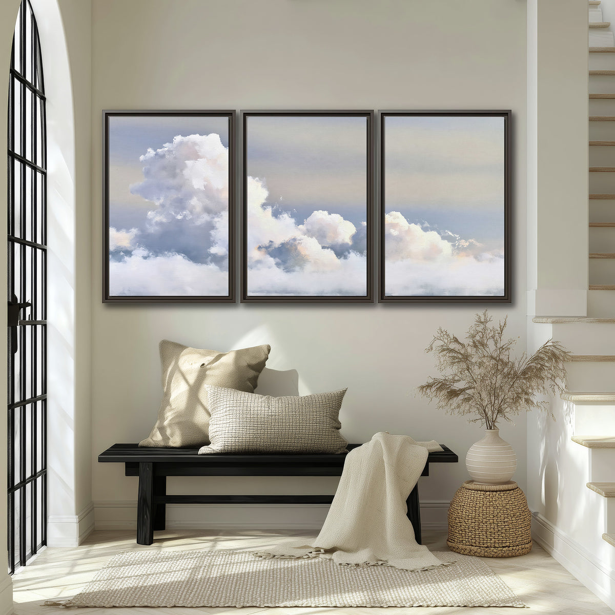 Large white clouds rising through a pale blue sky with gentle warm highlights 3 piece framed canvas wall art displayed in a entryway