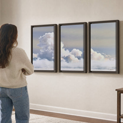 Large white clouds rising through a pale blue sky with gentle warm highlights 3 piece framed canvas wall art three panel arrangement on a wall