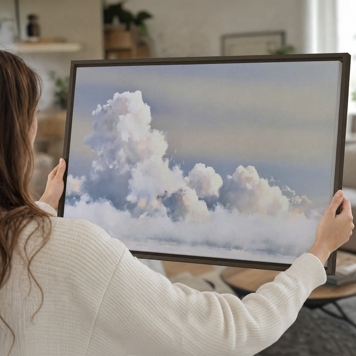 Large white clouds rising through a pale blue sky with gentle warm highlights single framed canvas wall art held in hands