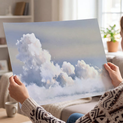 Large white clouds rising through a pale blue sky with gentle warm highlights single poster print held in hands