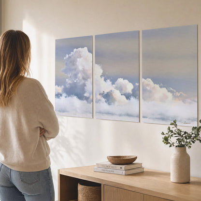 Large white clouds rising through a pale blue sky with gentle warm highlights set of 3 poster prints three panel arrangement on a wall