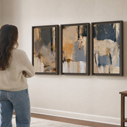 A pale unicorn emerging from loose vertical strokes of blue, ochre and cream 3 piece framed canvas wall art three panel arrangement on a wall