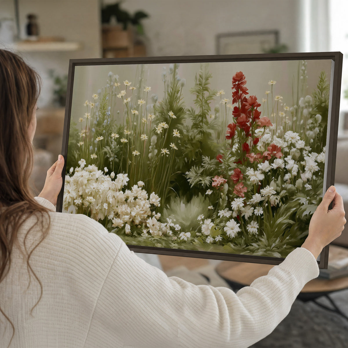 A soft meadow of white daisies and tall red blooms against a green background single framed canvas wall art held in hands