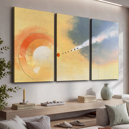 A warm orange circular form and diagonal pale streaks across a muted yellow and blue field 3 piece canvas wall art displayed in a console