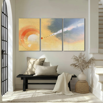 A warm orange circular form and diagonal pale streaks across a muted yellow and blue field 3 piece canvas wall art displayed in a entryway