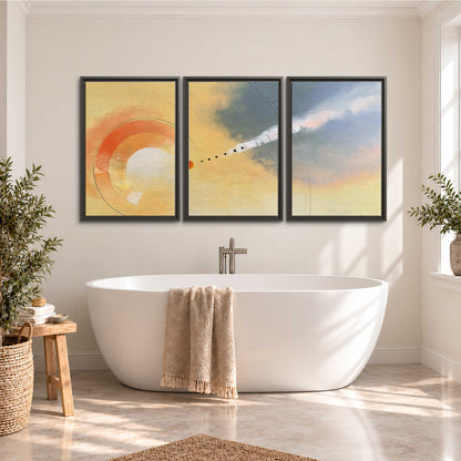 A warm orange circular form and diagonal pale streaks across a muted yellow and blue field 3 piece framed canvas wall art styled in an interior