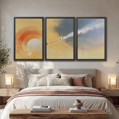 A warm orange circular form and diagonal pale streaks across a muted yellow and blue field 3 piece framed canvas wall art displayed in a bedroom